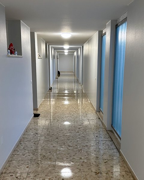 Flur mit spiegelndem Terrazzoboden, blauen Glasflächen und eingeschalteter Deckenbeleuchtung.