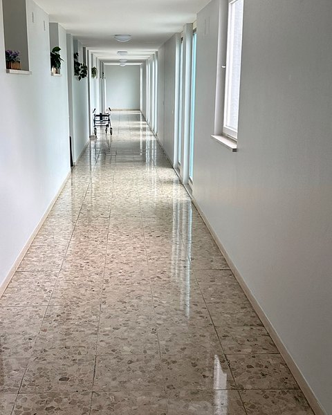 Langer, heller Flur mit glänzendem Terrazzoboden und Fenstern auf der rechten Seite.
